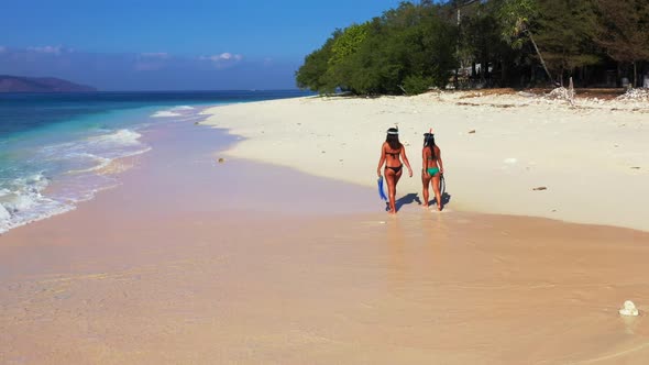 Women tanning on idyllic tourist beach wildlife by transparent ocean with bright sand background of 