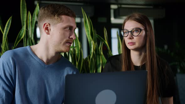 Man and a Woman Colleagues Who Communicate Sitting in Front of a Laptop