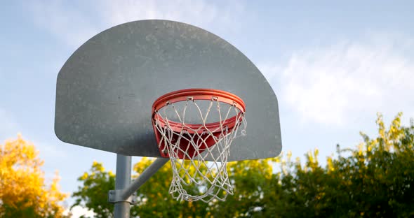 Close up shot of a basketball hoop with metal backboard, orange rim and a net in an empty park court