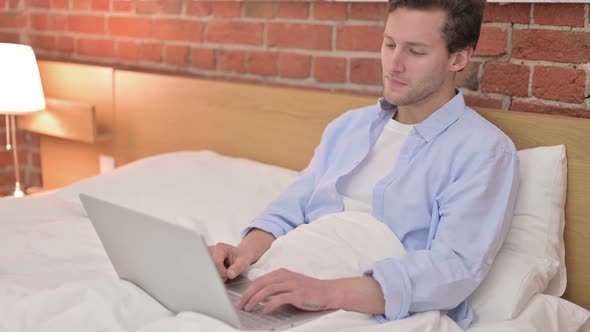 Young Man Doing Video Chat on Laptop in Bed