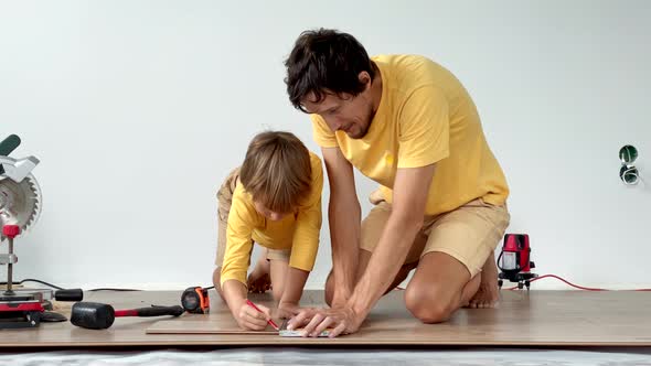 Father and His Little Son Install Laminate on the Floor in Their Apartment