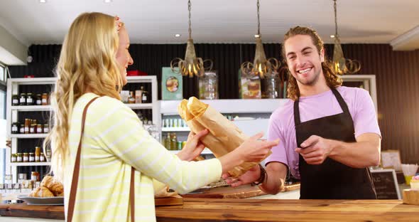 Waiter giving bread roll package to customer at counter