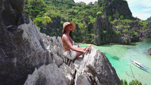 Woman In Sun Hat Sitting On Rocks Above Hidden Beach