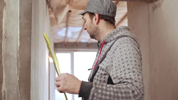 Middleaged Caucasian Male Worker Wearing Cap Using Tape Measurer Taking Gauge of Doorway in