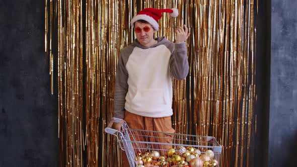 Male with Shopping Cart Filled of Assorted Baubles Near Wall with Golden Tinsel