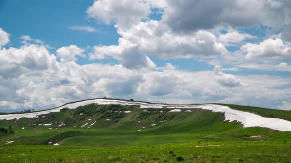 Time lapse over green meadow with snow drifts on ridge line in Utah