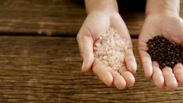 Hands holding sea salt and black pepper against wooden table 4k