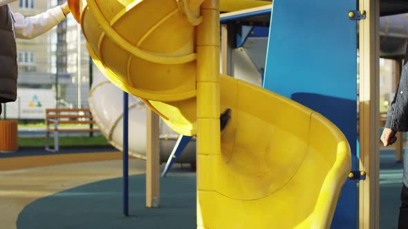 Happy Young Boy Coming down Spiral Slide in Urban Playground