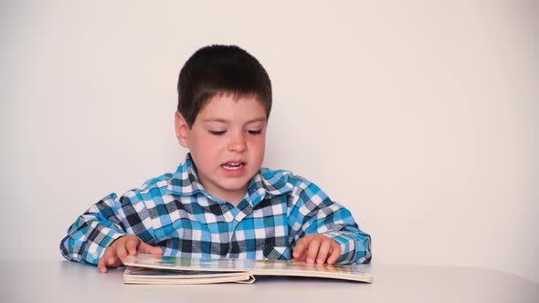 A 4Yearold Boy Looks at a Book with Thick Cardboard Pages with Pictures