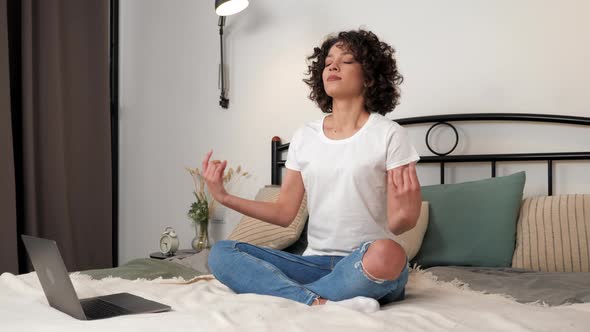 Smiling Curly Woman Sitting on Bed in Lotus Position After Hard Work at Laptop