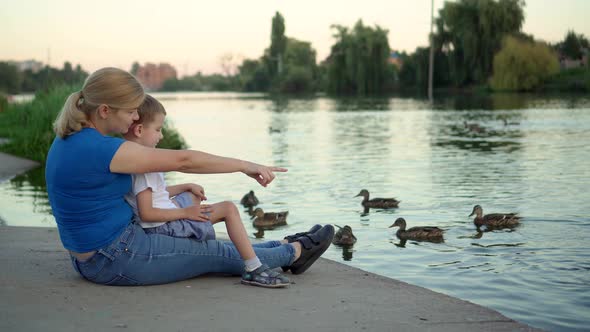 Mother and Child in Medical Masks Feed Ducks on the Lake
