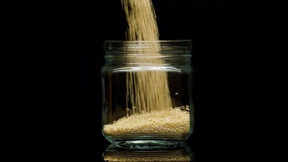 Closeup of Falling Down Quinoa Into Glass Jar on Black Background