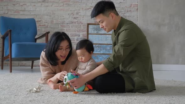 Young Mom and dad sit on the floor room inside the house and play with child.