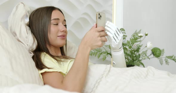 Girl with Bionic Arm Using Phone Reading Social Media and Chatting in Bed Woman with Disability