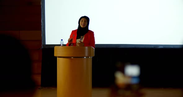 Mature Caucasian hijab businesswoman speaking at podium in auditorium 4k