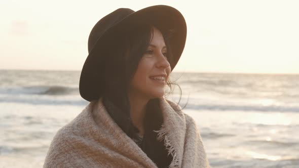 Portrait of Romantic Brunette Woman in Hat and Coat Walking on the Beach in Autumn at Sunset or