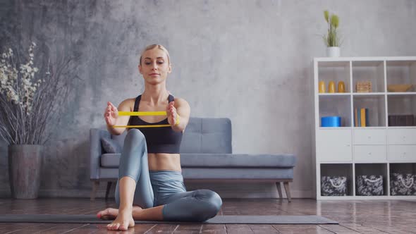 Young and sporty girl in sportswear is doing exercises in home interior using resistance band.