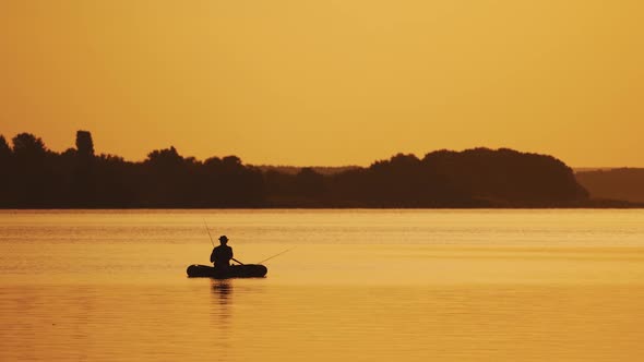 Amazing view of the evening sunset and a man in a boat fishing. Silhouette of a fisherman