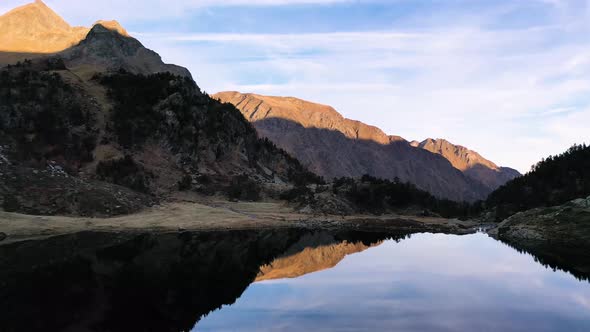 Reflecting calm Lac d'Espingo lake in Haute-Garonne, Pyrénées mountains, France with sun hitting the