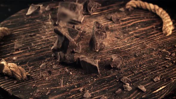 Super Slow Motion Falling Pieces of Dark Bitter Chocolate on a Wooden Board