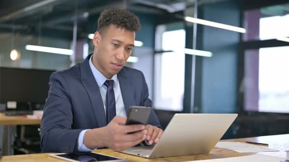 Cheerful Young Businessman Using Smartphone in Office