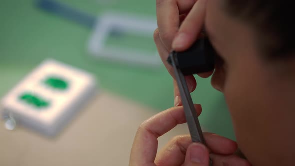 Closeup Face Concentrated Expert Appraiser Examining Gemstone in Tweezers with Magnifier