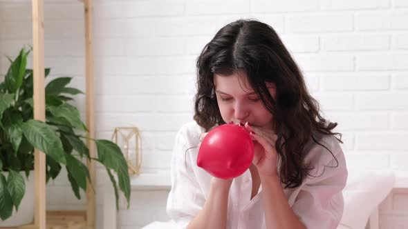 Girl is Blowing Air Balloon at Home Handsome Brunette Girl Inflating Red Heart Shaped Balloon