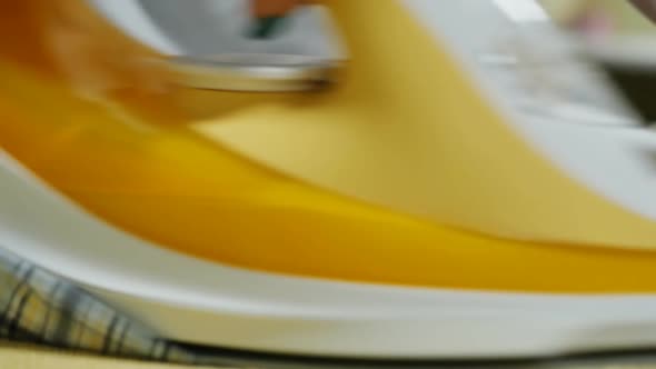 Female Hands Ironing a Plaid Shirt with a Yellow Iron