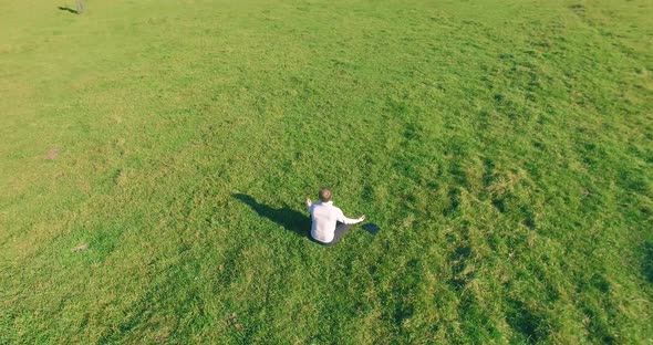 Low Orbital Flight Around Man on Green Grass with Notebook Pad at Yellow Rural Field