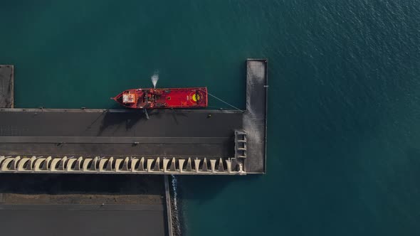 Red cargo ship anchored at quay of Tazacorte harbor in La Palma island. Aerial top-down sideways