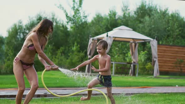 Mom and Son Playing on the Lawn Pouring Water Laughing and Having Fun on the Playground with a Lawn