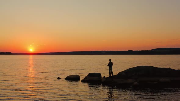 People fishing in the evening. Fishermen stand on a big stone surrounded by water at sunset. 