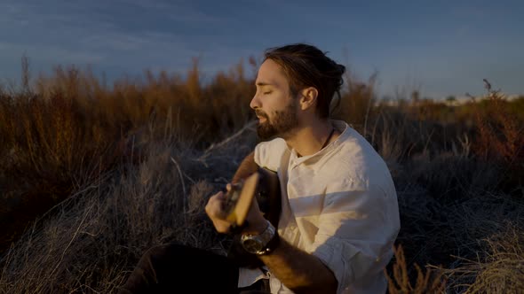 Man Musician Playing the Guitar and Singing at Sunset Field in Autumn