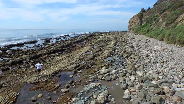 Tracking shot of a young man running on a rocky ocean beach shoreline