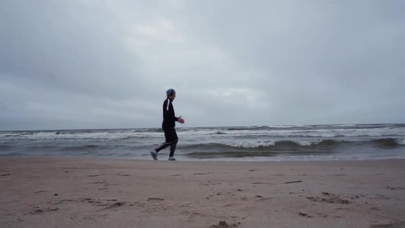 young man is in the beach. he stops running and begins to jump in the water of the sea. he looks hap