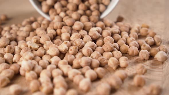 A bunch of chickpeas are poured out of a white ceramic cup onto the wooden surface 