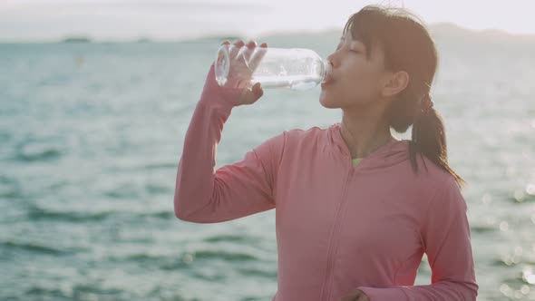 Woman runner drinking water while standing seaside.