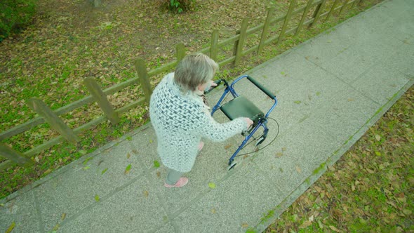 Hunched Grandmother Strolls Near Fence Using Walking Frame