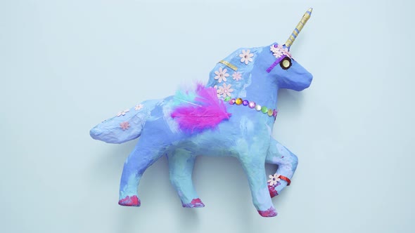 Kids craft. Painted blue and decorated with jewels and feathers paper mache unicorn.