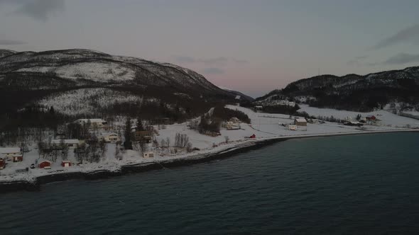 Snowy Arctic Village With Oceanfront Houses During Polar Night In Norway. - aerial