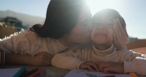 Asian mother kissing her son and smiling in camera