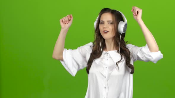 Brunette Listens Through the Headphones with Energetic Music and Builds Grimaces. Green Screen