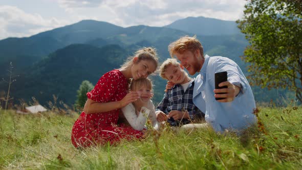 Positive Family Taking Selfie on Cellphone Sitting Green Grass Mountain Hill