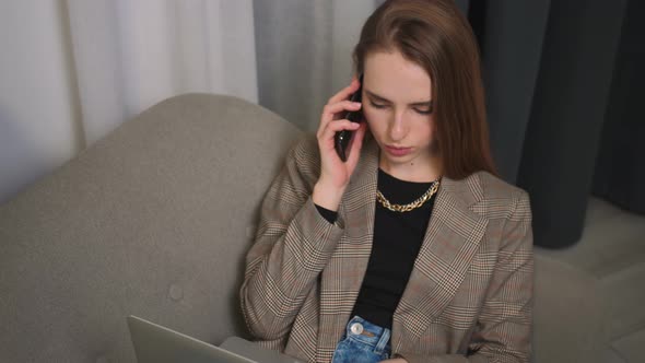 Portrait of Focused Businesswoman Talking on a Mobile Phone While Working on a Laptop