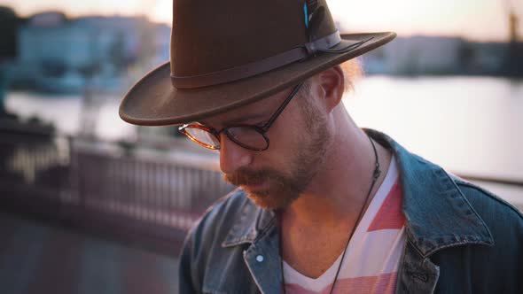 Colorful Portrait of Young Stylish Guy with Red Beard in Glasses and in Hat Looking at Camera During