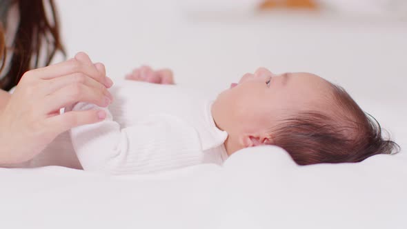 New asian mom playing to adorable newborn baby on bed smiling and happiness at home.