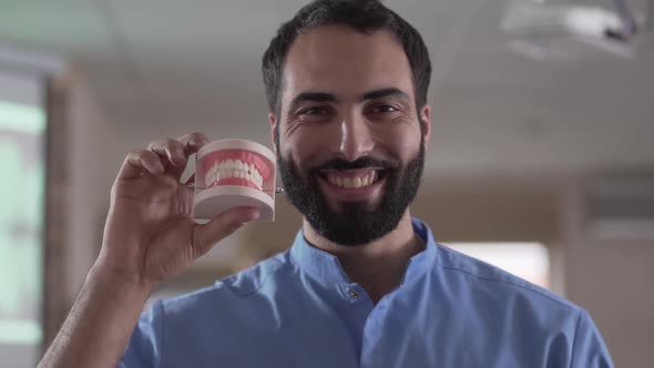 Close-up Portrait of Young Middle Eastern Man Holding Teeth Cast and Smiling at Camera. Professional