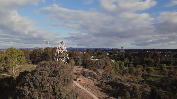 Wide circling drone shot of Victoria Hill Mining Reserve poppet head in Bendigo. Radio tower and a s