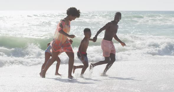 Smiling african american family holding hands and running on sunny beach