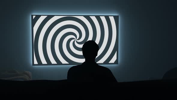 Darkroom with person watching TV with a hypnotic spiral on the screen. 4K render